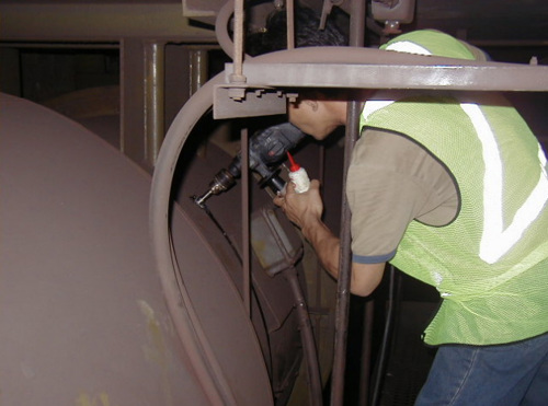 A man in a high-vis vest drilling an access hole for conduit into a machine
