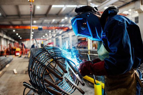 Man in protective gear welding a metal cage inside of a factory